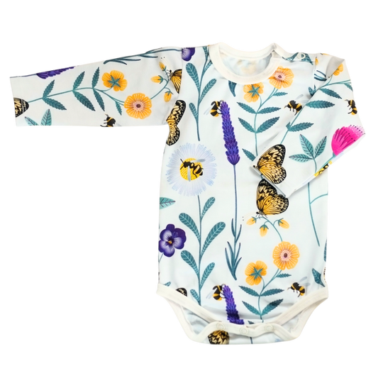 Baby body i vit ekologisk bomullsjersey med färgglatt mönster av blommor och insekter i lila, rosa, gult och turkos. Knäppning vid axel och gren.